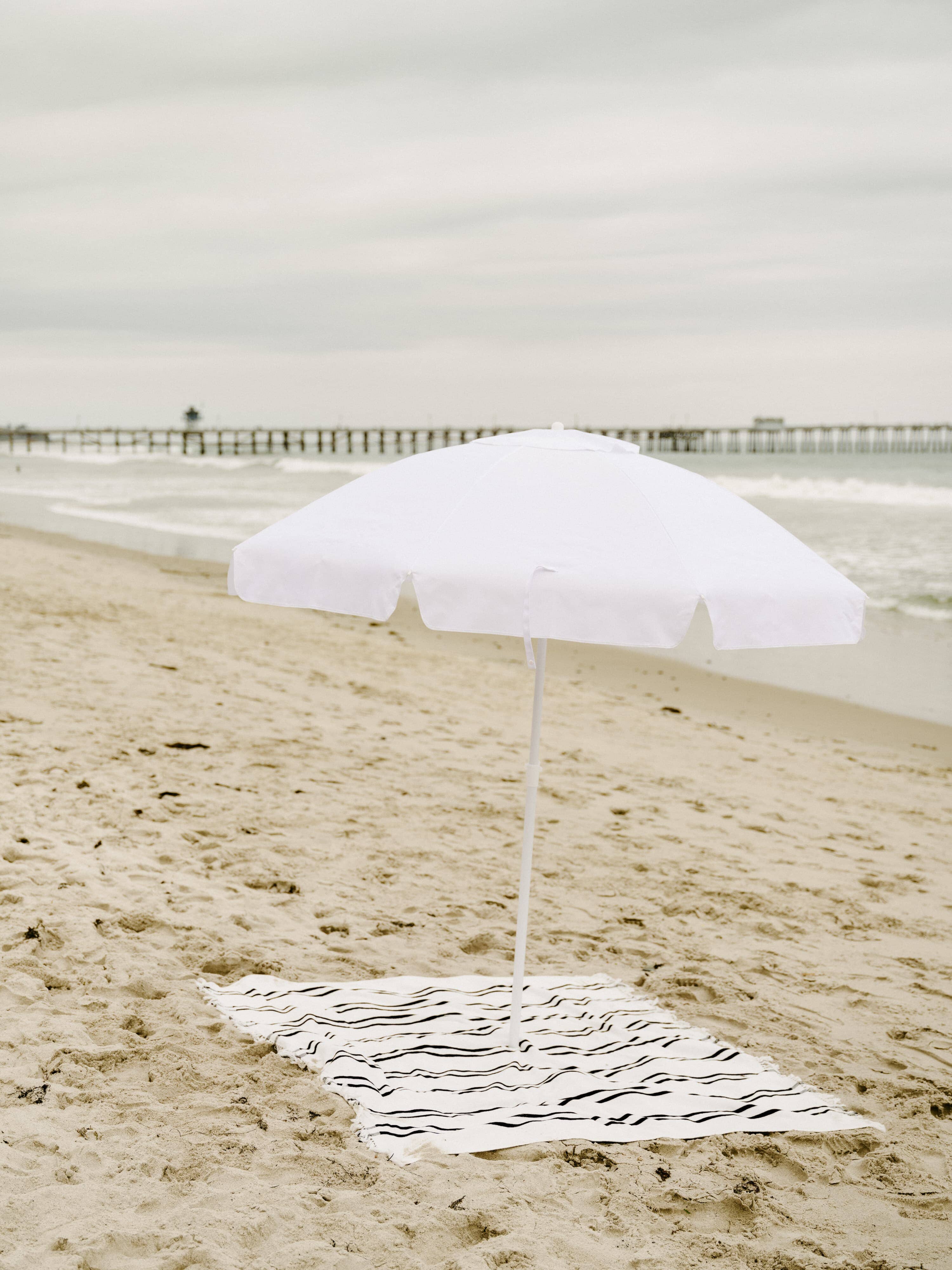 White family umbrella at the beach with beach blanket