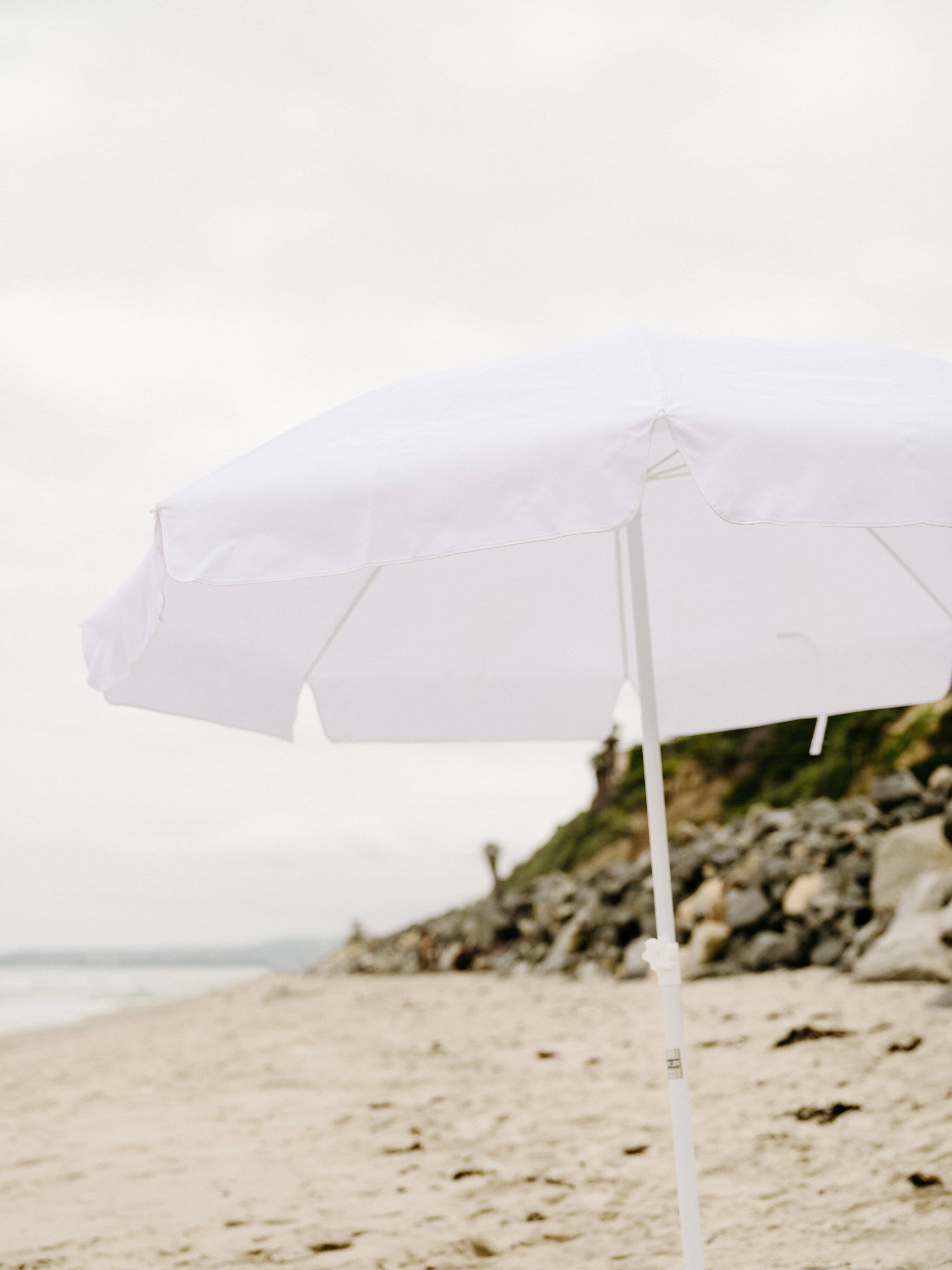 White family umbrella at the beach with beach blanket