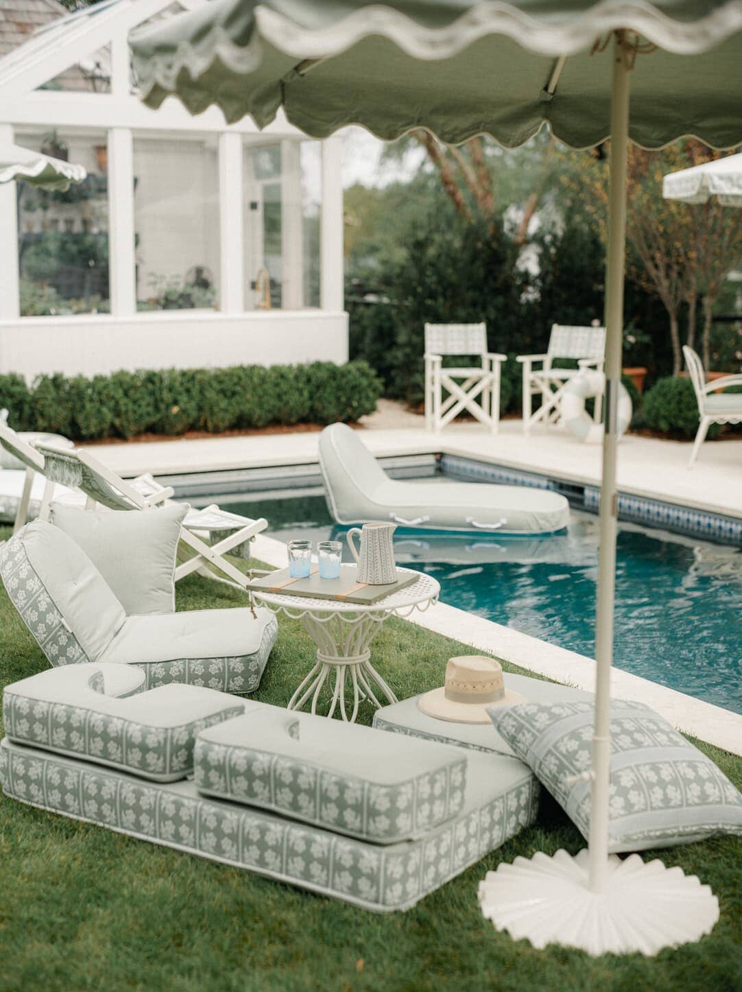 Backyard pool area with outdoor pillow stack, umbrellas, and reclining lounger