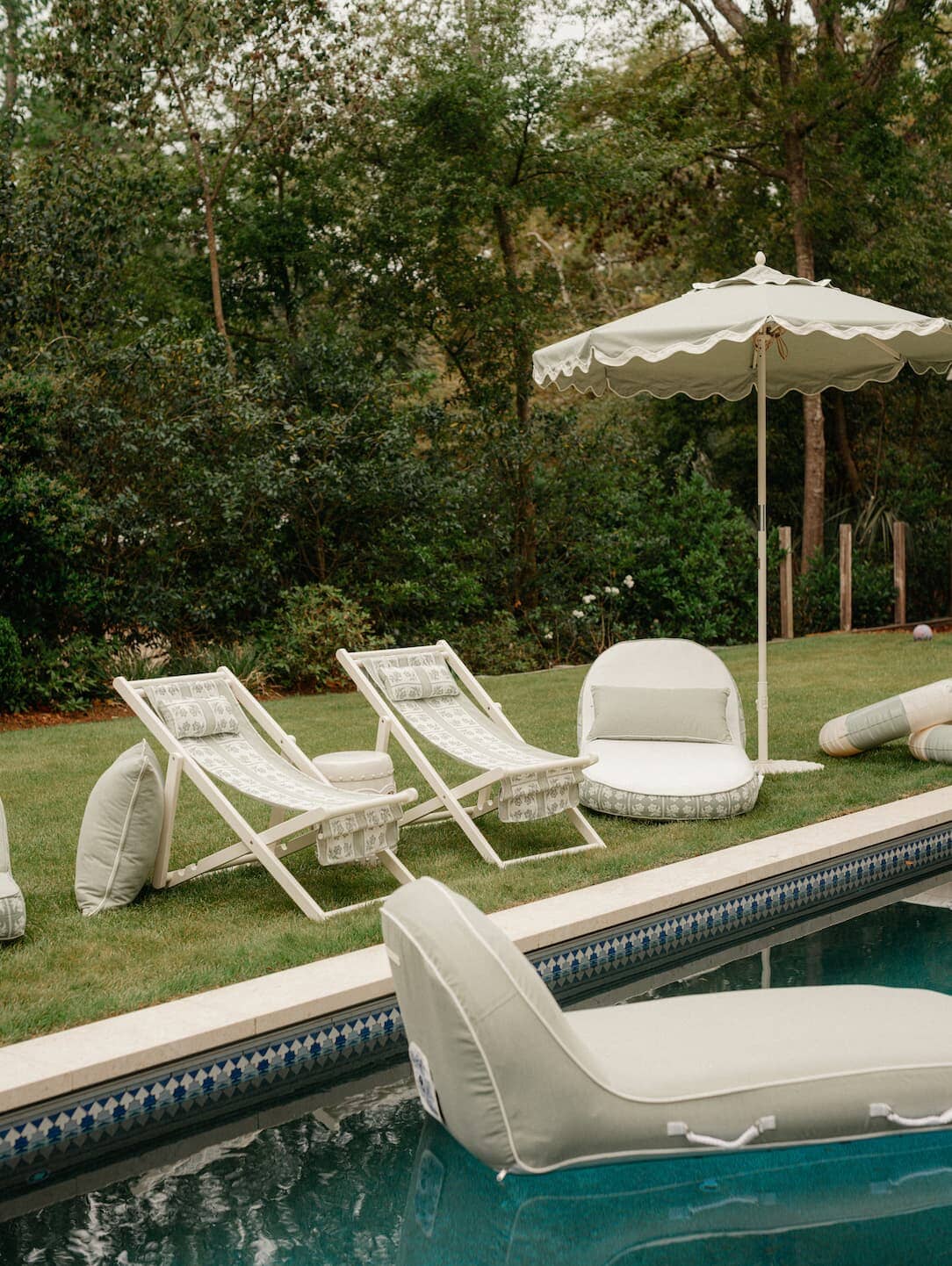 Sling chairs, and umbrella on the grass next to a pool