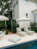 Sun lounger, umbrella and floor pillow next to a pool