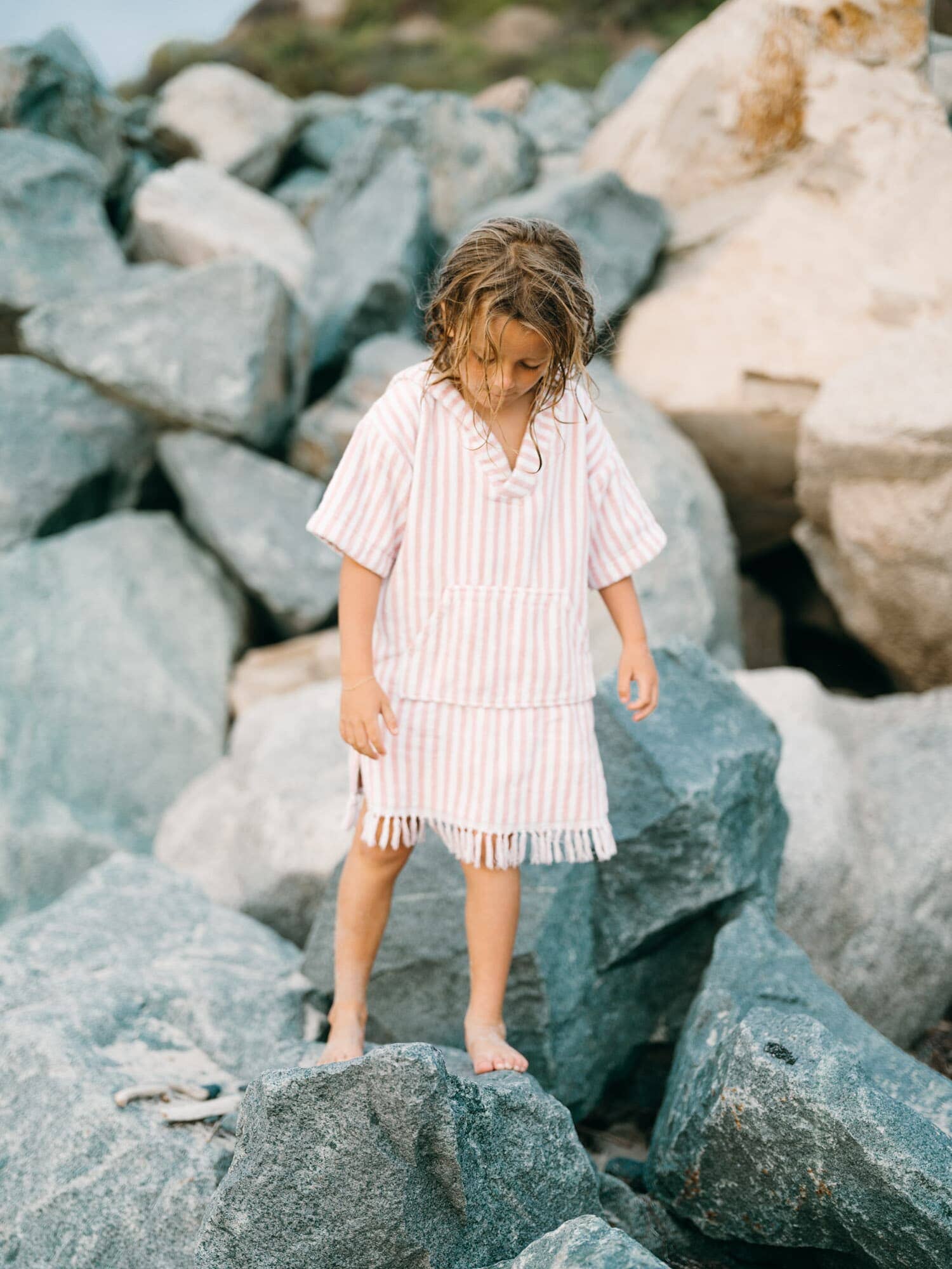 Child in pink poncho playing on rocks