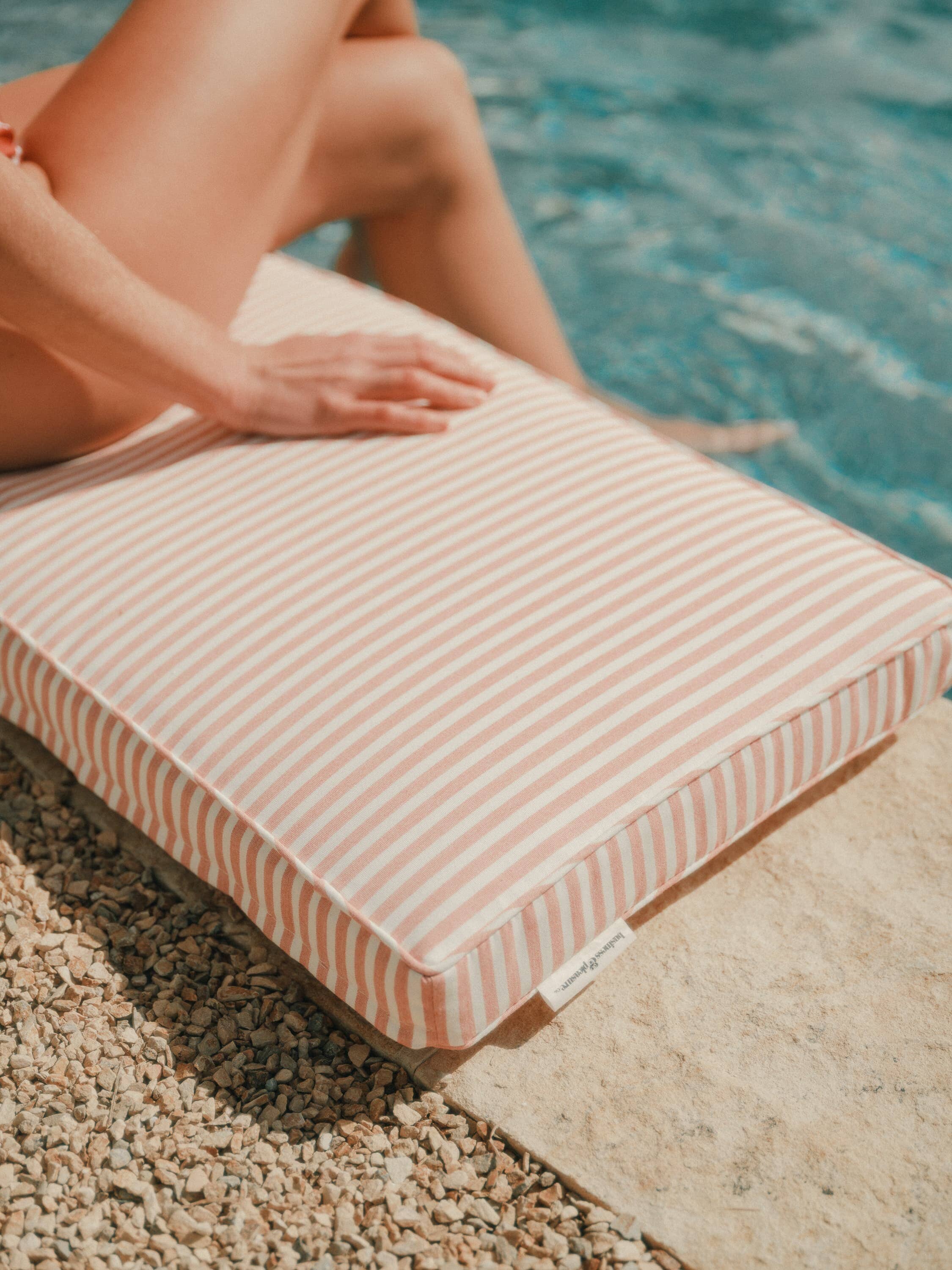 Person sitting on a bench pillow next to a pool
