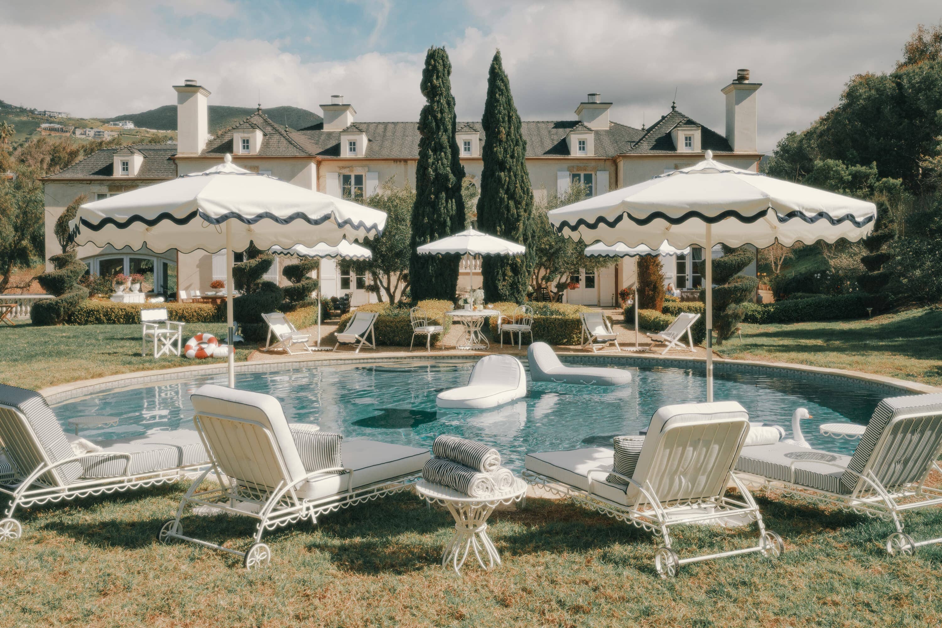 Pool setting with white navy sun loungers, white umbrellas and pool floats