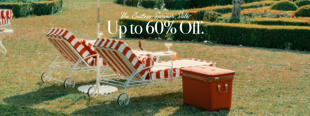 Outdoor lawn scene with red-and-white striped lounge chairs, a small white side table, and a rust-orange cooler, with overlaid sale text reading 'The Endless Summer Sale. Up to 60% Off.