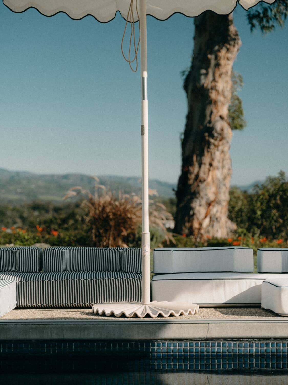 white clamshell base next to a pool with an umbrella and cushions