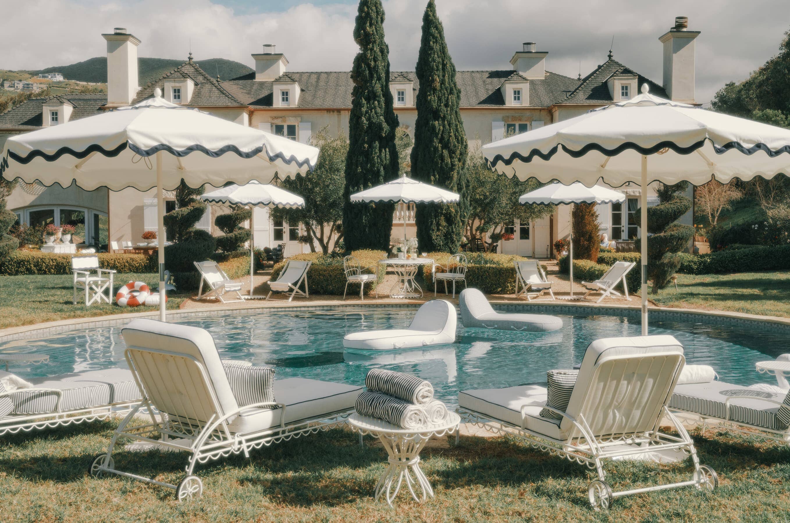 Outdoor pool setting woth riviera white umbrellas, chairs and pool floats