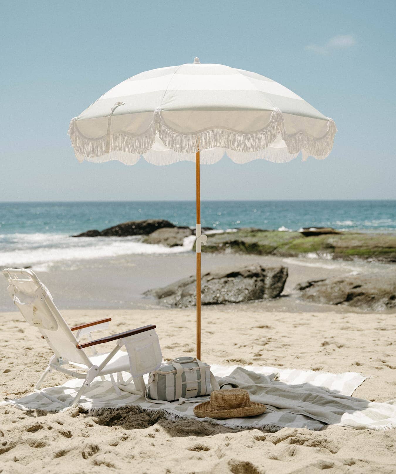 white holiday tommy chair, sage blanket and sage umbrella on a beach