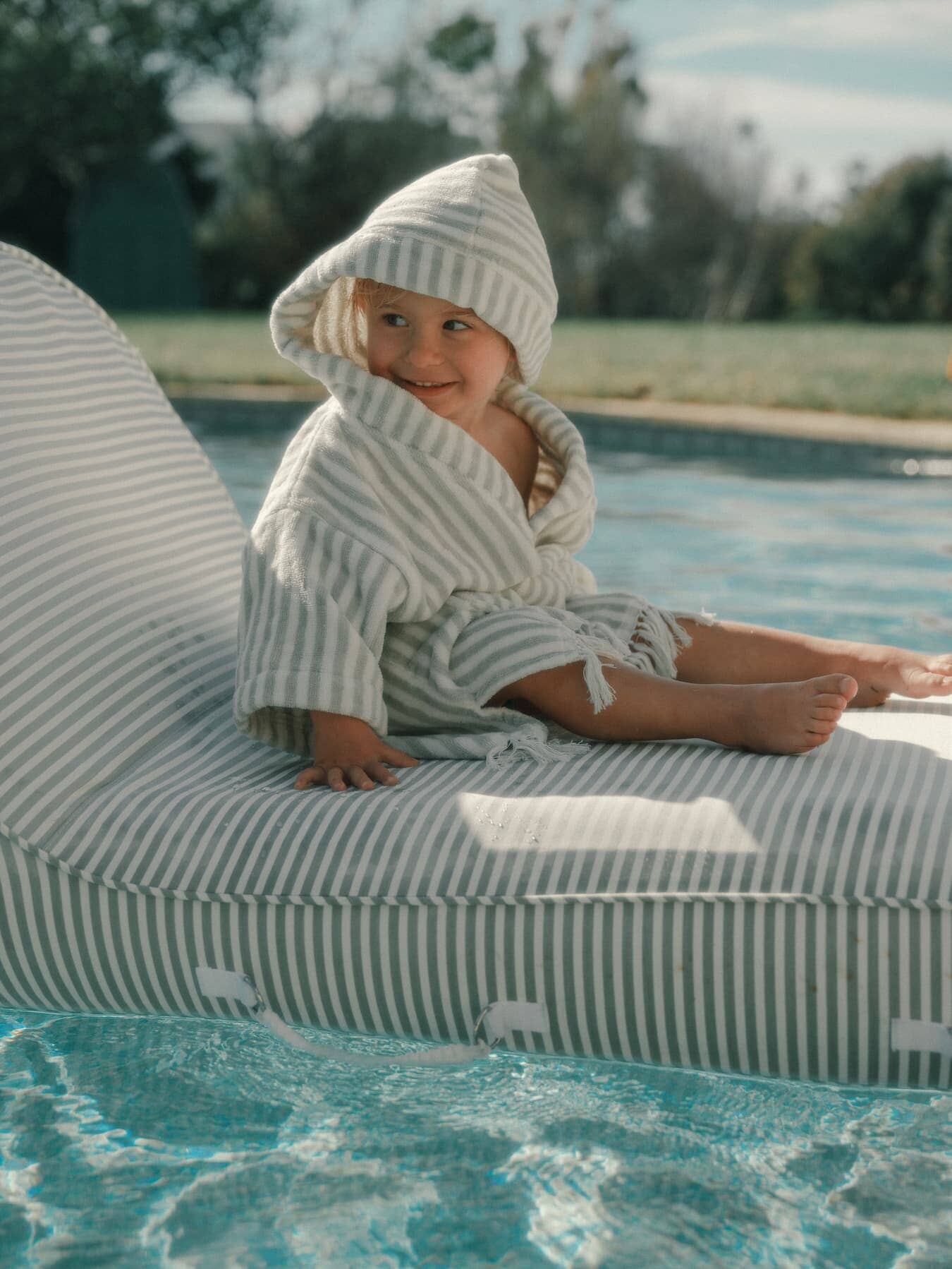 little boy sitting on a pool lounger wearing the sage poncho