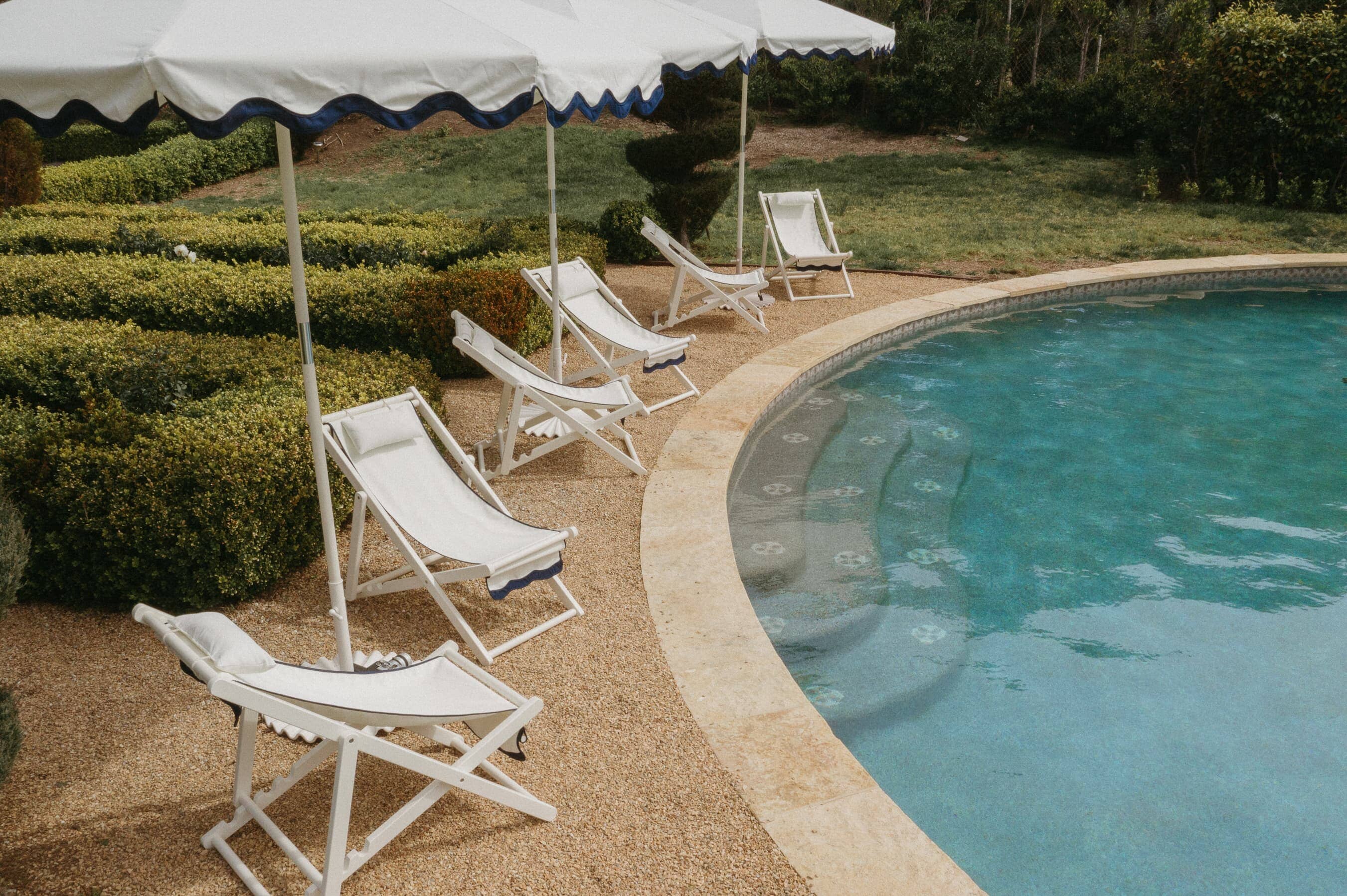 pool setting with riviera white sling chairs and market umbrellas